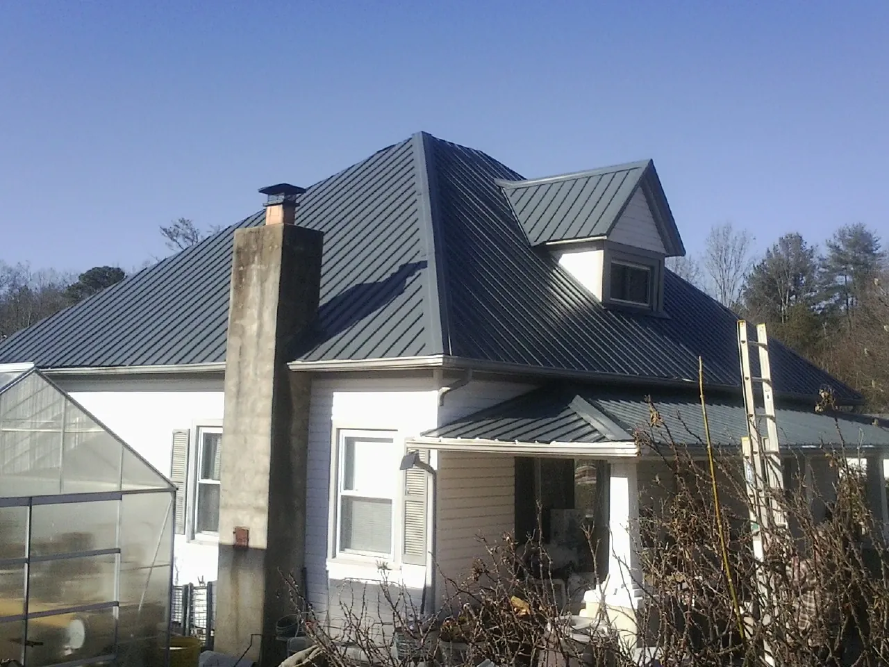 Dark blue standing seam metal roof on a white farmhouse with dormer — Slate & Tile Roof Repair by Roofing Brothers in Crosby