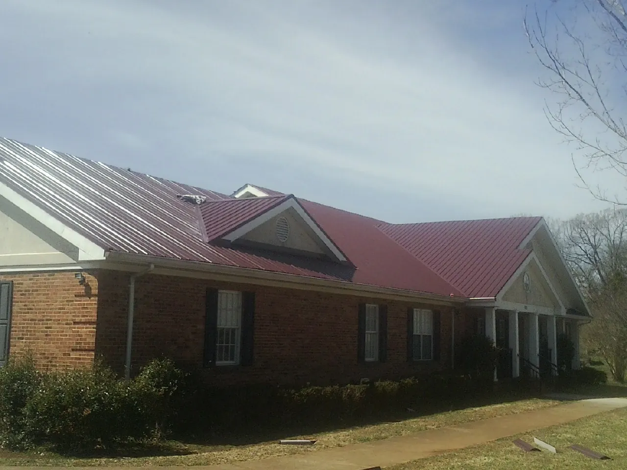 Red metal roof with gabled entries on a long brick building, from a Hail Damage Roof Repair job in Crosby