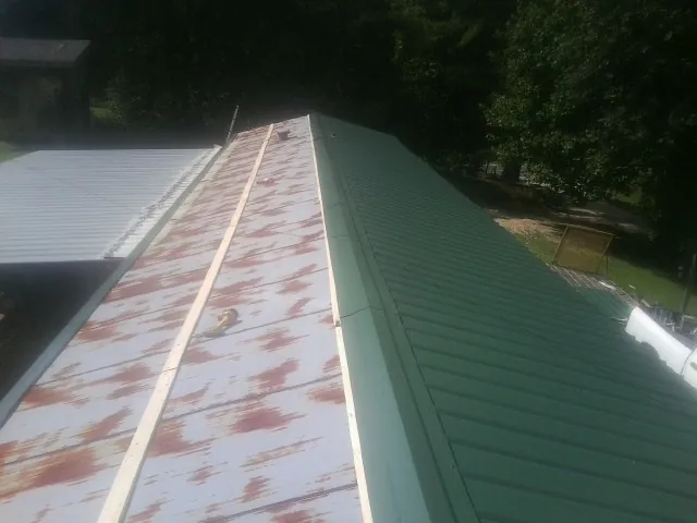Old rusted panels beside newly installed green metal roofing — Wind Damage Roof Repair by Roofing Brothers in Crosby