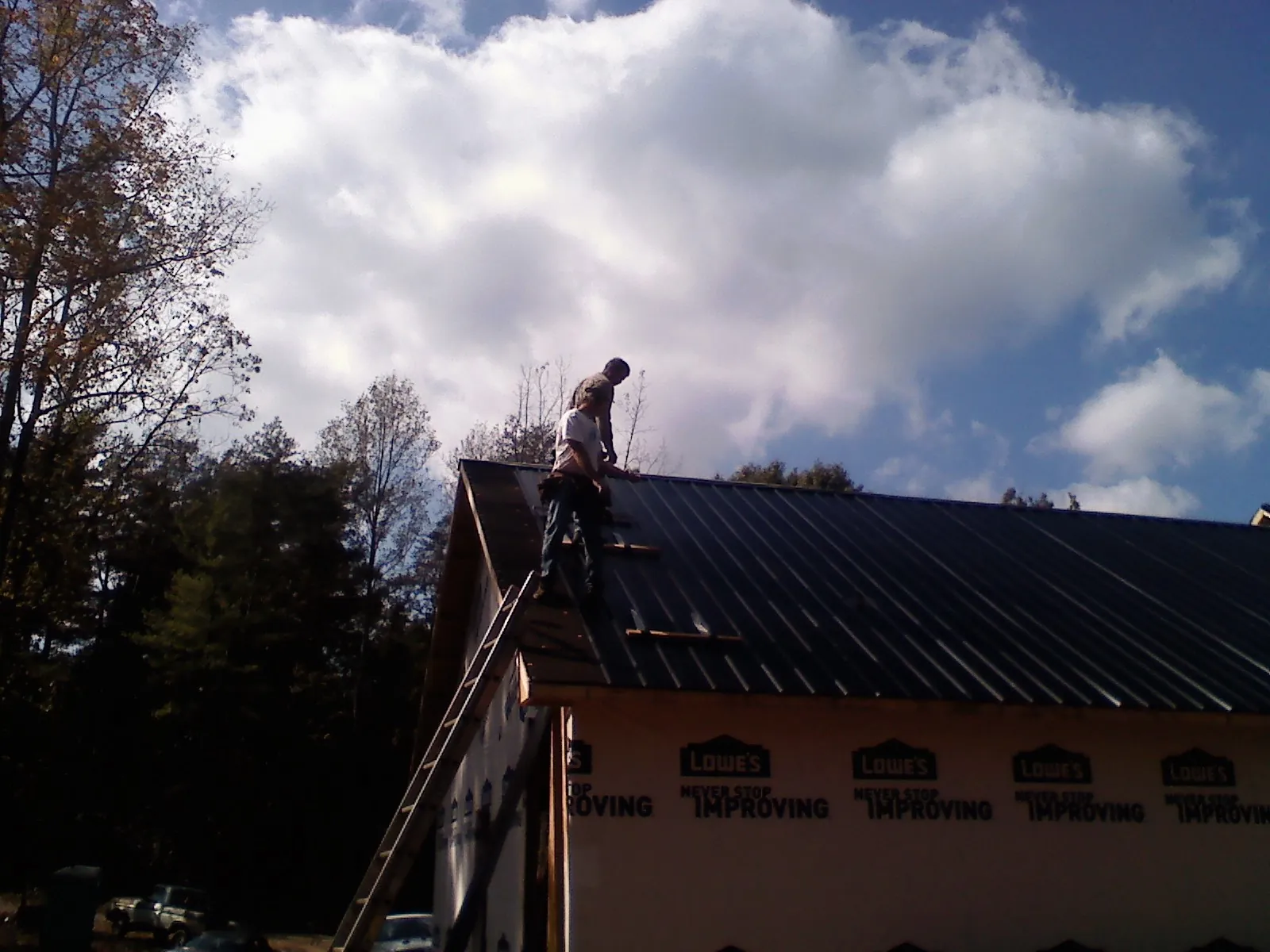 Roofer fastening dark metal panels high against a cloudy sky, from a Roof Inspection job in Crosby