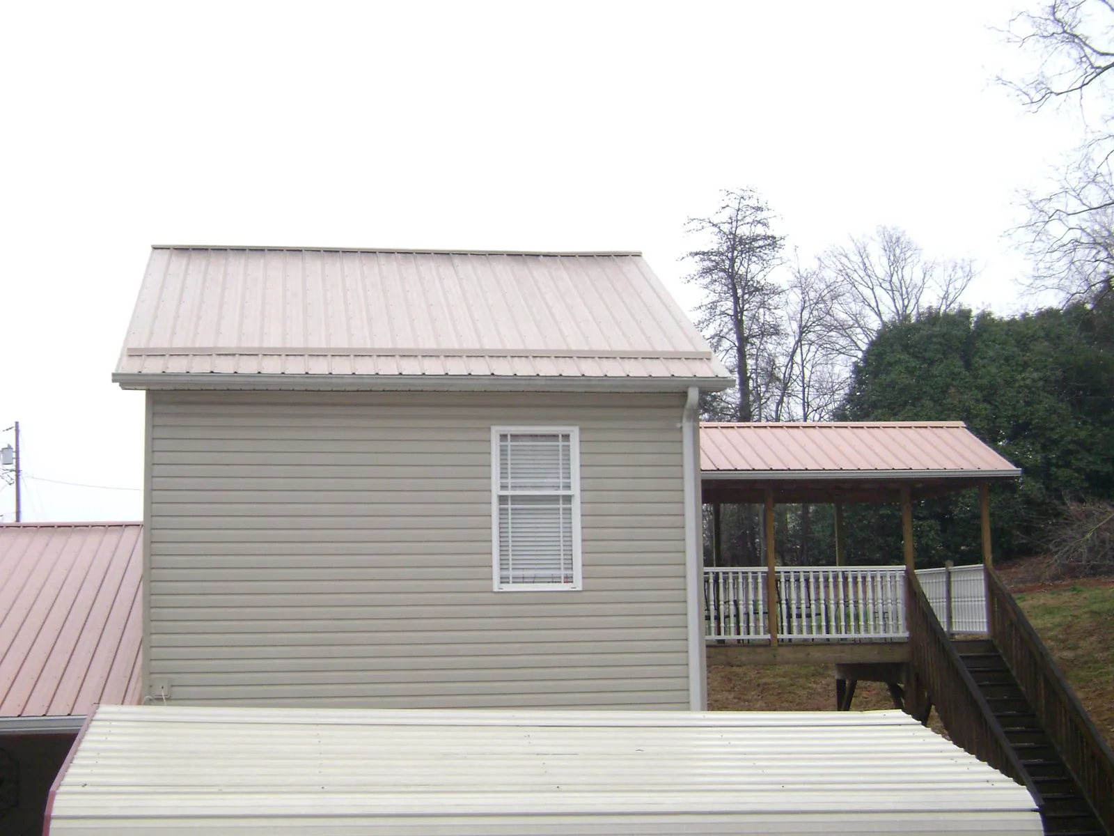 Tan metal roofs on a two story addition and attached porch, from a Roof Replacement job in Crosby
